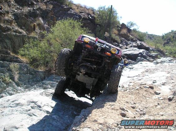 Red off-road truck tilted on rocky terrain, front grille visible with yellow lights
