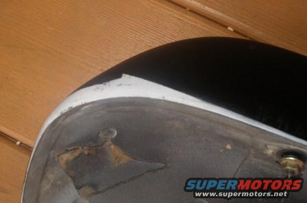 Black car fender with white trim, showing underside with rust and a bolt