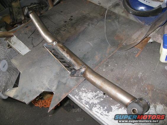Metal suspension component with welded brackets and rubber bushing on a workbench
