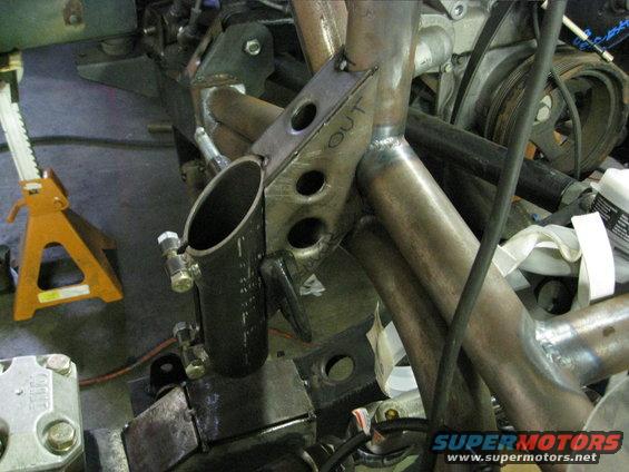 custom metal tubing welded together, with 'OUT' written on a bracket. Engine parts visible in background