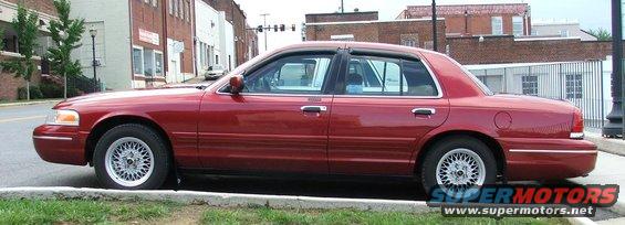 Red sedan parked curbside, side view. Aftermarket wheels visible