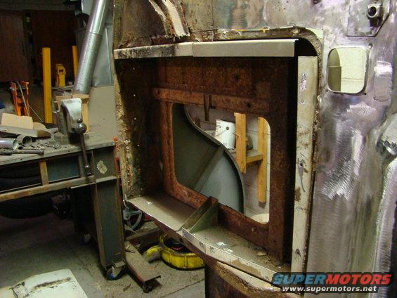 Rusted vehicle body section with large opening, showing interior structure and workshop background