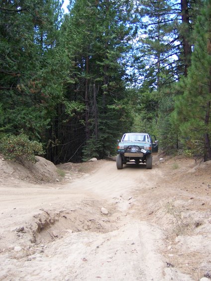 Light blue SUV with aftermarket bumper on a dirt road in a forest