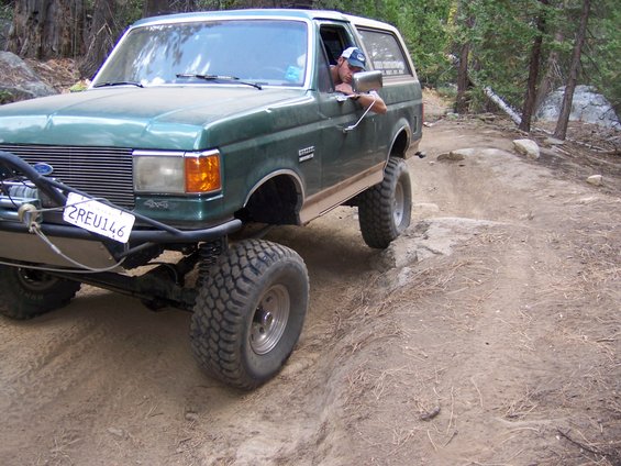 Green 1991 Ford Bronco off-roading on a dirt trail, front 3/4 view