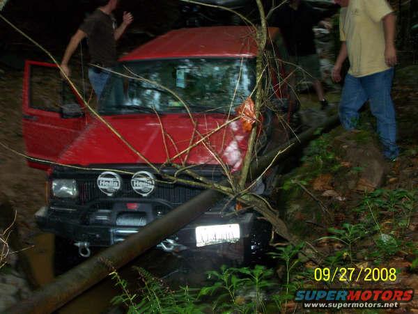 Red 1992 Jeep Cherokee stuck off-road with branches on windshield