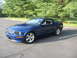 2007 Ford Mustang - A blue 2007 Ford Mustang coupe is shown from a three-quarter front view in a parking lot with trees in the background.