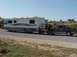 2002 Ford Supercrew - A gray pickup truck tows a large RV down a highway, with a person standing beside the truck.