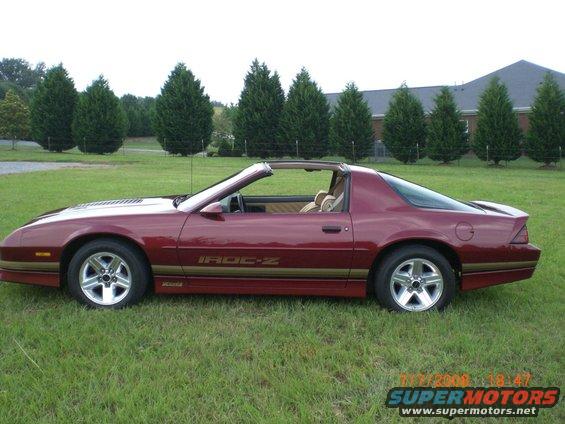 Maroon Chevrolet Camaro IROC-Z t-top, side view, parked on grass with trees and a building in the background