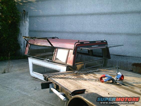 Two truck bed caps, one red and one white, are chained to a flatbed trailer