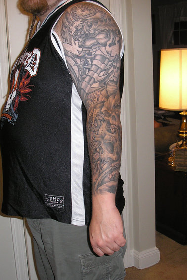 Person's arm with a full sleeve tattoo of a mask and skulls