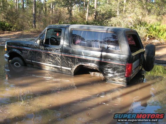 Black Ford Bronco stuck in muddy water, side view, spare tire mounted on rear