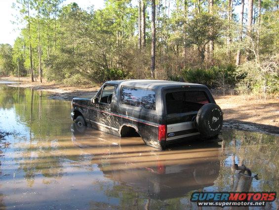 Black 1994 Ford Bronco stuck in muddy water, rear-mounted spare tire visible