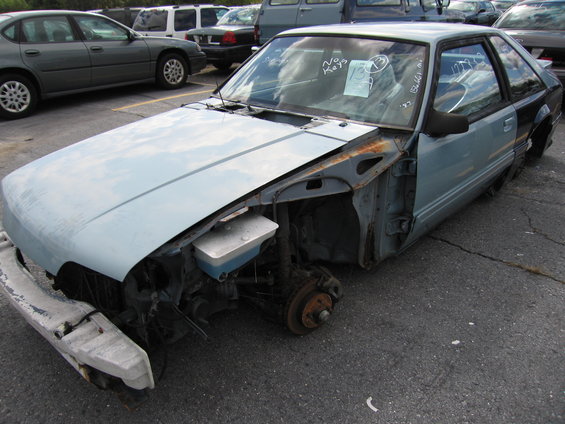 Light blue coupe missing front bumper, hood, and one front wheel. Paper on windshield says "No Keys"