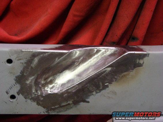 Vehicle frame section with metal grinding and weld repair, red cloth in background