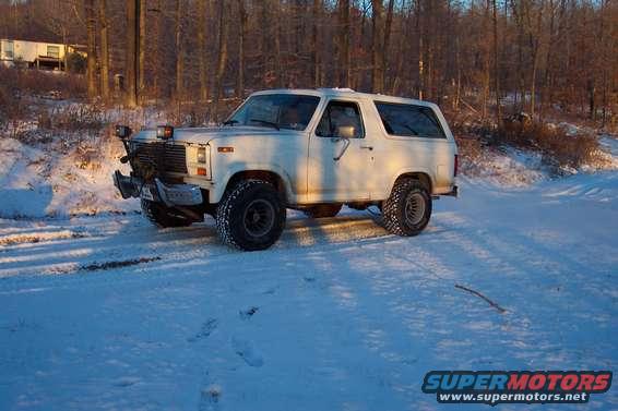 White SUV with a brush guard and off-road tires parked in snow