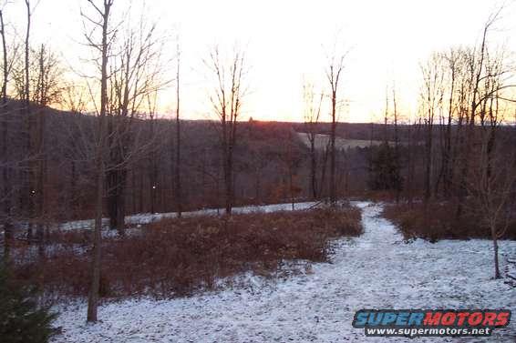 Winter landscape with snow on the ground and bare trees against a sunset sky