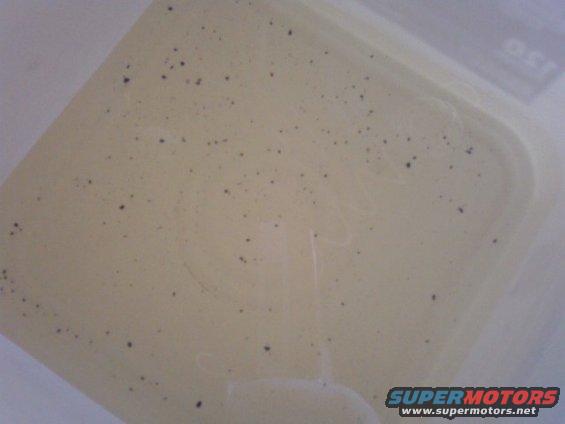 plastic coolant reservoir with dark specks inside, supermotors.net logo at bottom right