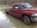 1996 Dodge 1500 - A red pickup truck is stuck in a muddy puddle, with its rear wheel submerged.
