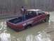1996 Dodge 1500 - A person stands in the bed of a red pickup truck that is stuck in a large mud puddle in a wooded area.