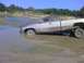 1996 Dodge 1500 - A 1996 Dodge 1500 pickup truck is stuck in a muddy body of water, with trees and a sandy embankment in the background.