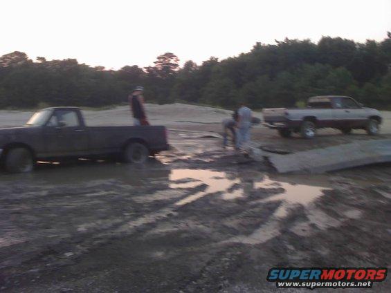 Two pickup trucks stuck in mud with people around them