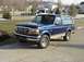 1996 Ford Bronco - A blue 1996 Ford Bronco is parked on a paved surface in front of a suburban neighborhood.