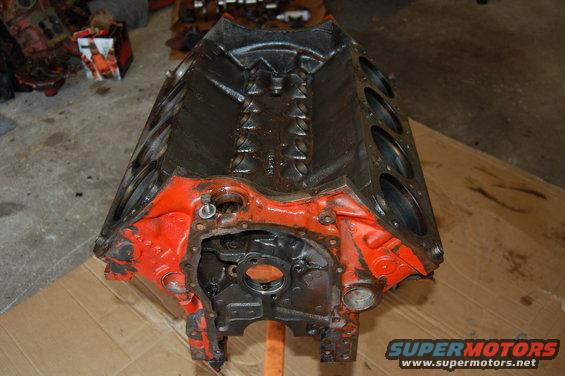 Orange and black engine block on a wooden surface. Other engine parts are visible in the background