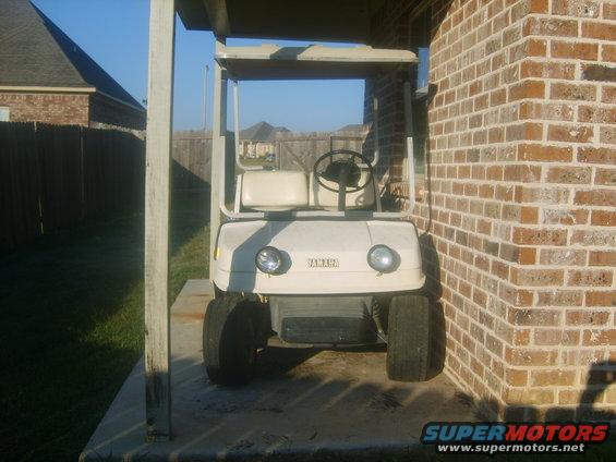 White Yamaha golf cart parked under a covered patio next to a brick wall