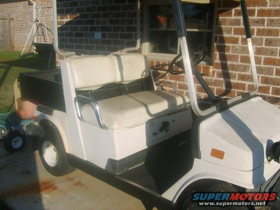 White golf cart with two rows of seats and a black cargo bed in the back