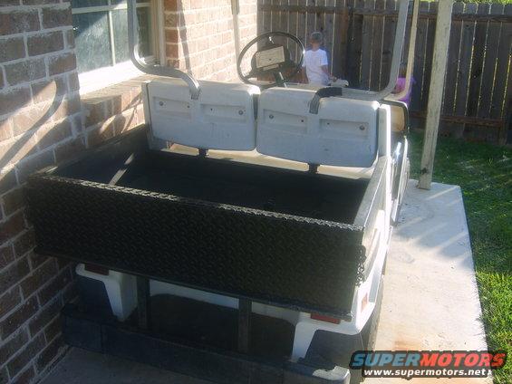 Golf cart with a black diamond plate utility bed, white seats, and a steering wheel