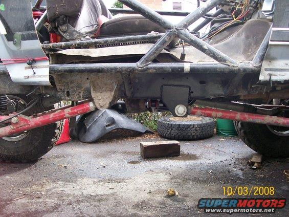 Modified vehicle chassis with red suspension components, a spare tire, and a black plastic fender on the ground