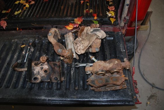 Rusty brake calipers and brackets in a truck bed with fallen leaves