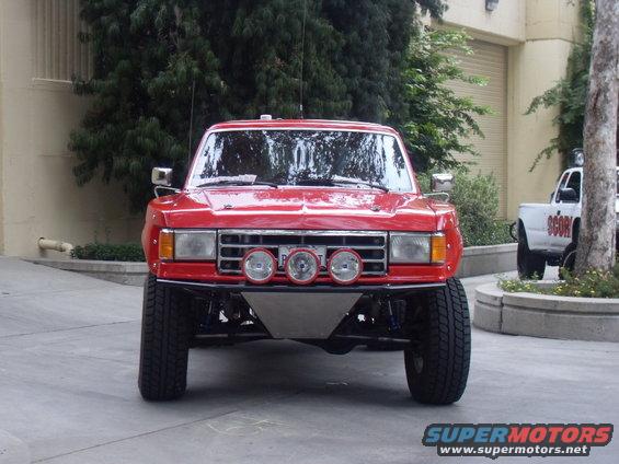 Red off-road truck, front view, with three spotlights and a skid plate