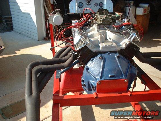 Engine assembly on a red metal stand, with exhaust headers and carburetor visible