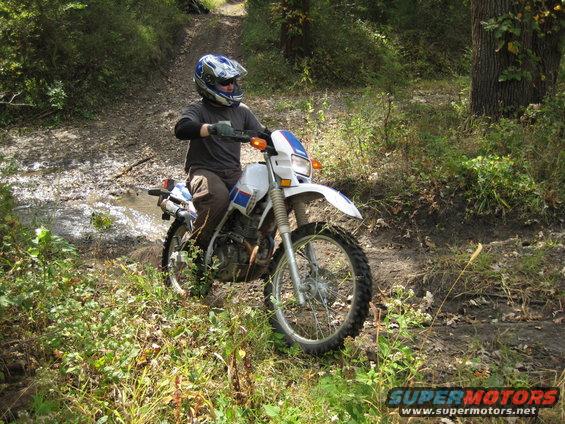 Guy in helmet riding a dirt bike through a muddy, wooded trail