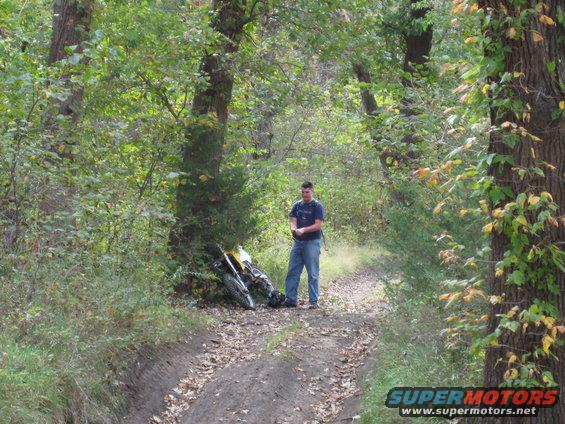 Yellow and black dirt motorcycle lying on its side on a dirt path in a wooded area