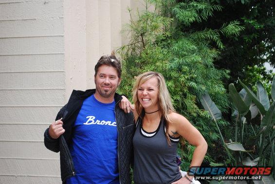 Man in blue Bronco t-shirt and woman in grey tank top pose in front of building and plants
