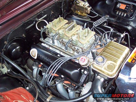 Engine bay with three carburetors, black valve covers, and a gold coolant overflow tank