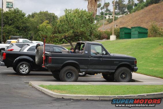 Black 1996 Ford Bronco parked next to a black pickup truck, spare tire on rear