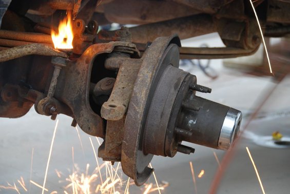 Rusted vehicle suspension component being heated by a torch, with sparks flying