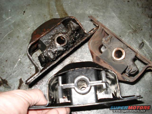 Three used engine mounts, one held by a hand, on a metal surface