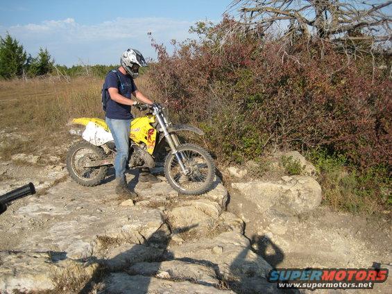 Yellow 1993 Suzuki RMX250 dirt bike on rocky terrain with a rider wearing a helmet