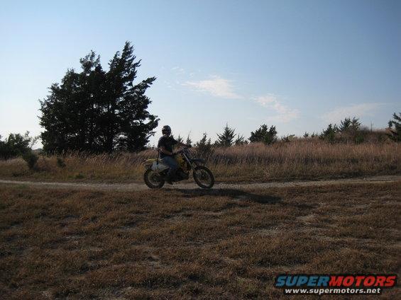 Dirt bike rider on a dirt road with dry grass and trees