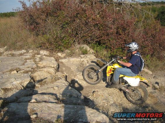 Yellow dirt bike with rider on a rocky trail, rider wearing a helmet and backpack