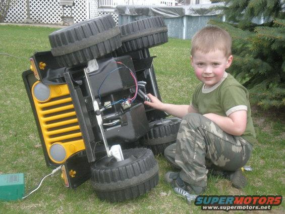 Kid kneeling next to a toy jeep that's on its side, looking at the wiring