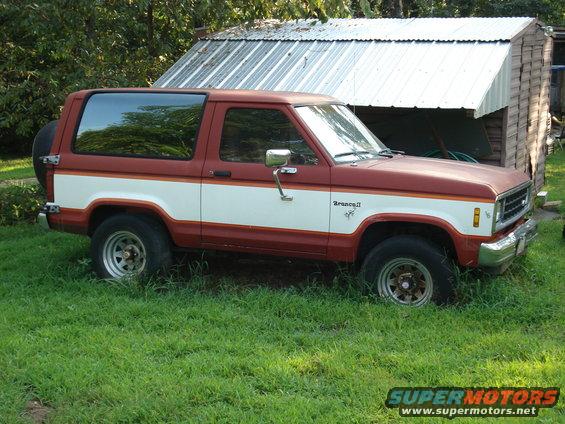 Red and white two-door Ford Bronco II parked in grass, spare tire on rear door