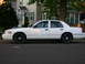2000 Ford Crown Victoria - A white 2000 Ford Crown Victoria sedan is seen from the side, parked on a residential street.