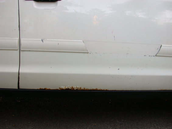White car door with rust along the bottom edge and damage to the trim