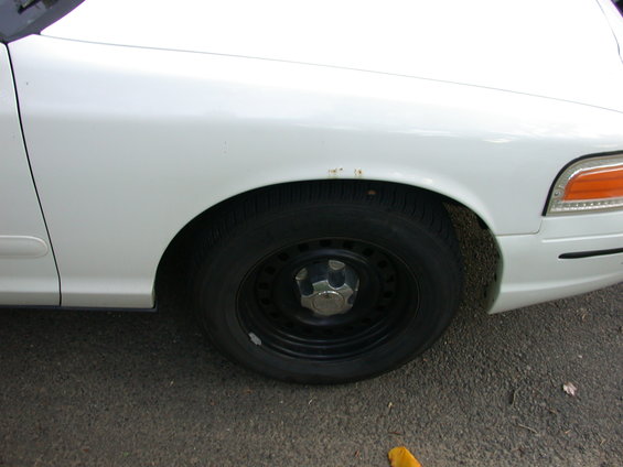 White 2000 Ford Crown Victoria front fender and wheel with some rust spots