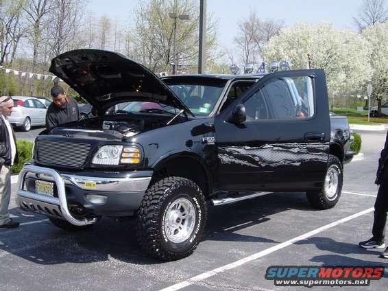 Black Ford F-150 pickup truck with hood and driver door open, aftermarket wheels, and bull bar
